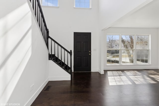 foyer entrance with wood finished floors, visible vents, baseboards, a high ceiling, and stairs