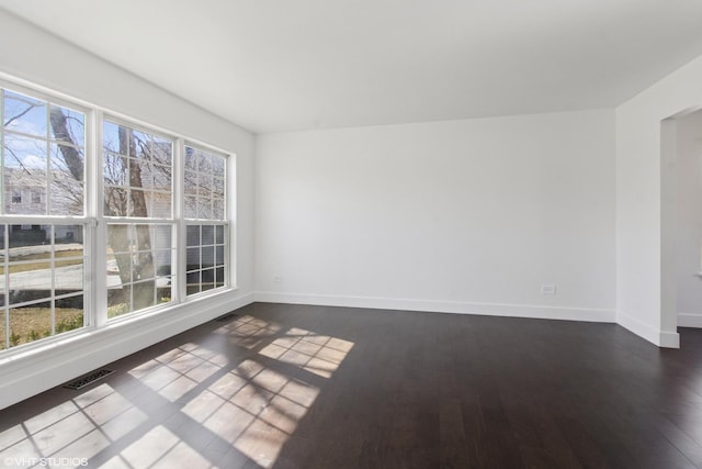 unfurnished room featuring dark wood-style floors, visible vents, and baseboards