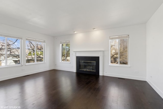 unfurnished living room featuring visible vents, baseboards, dark wood-style floors, and a tiled fireplace