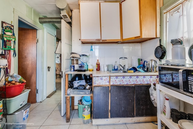 kitchen featuring light tile patterned floors, decorative backsplash, stainless steel microwave, and light countertops