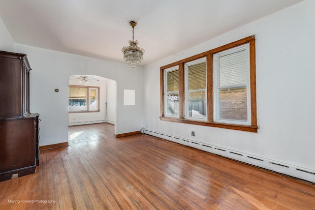 unfurnished room featuring wood-type flooring, arched walkways, baseboards, and baseboard heating