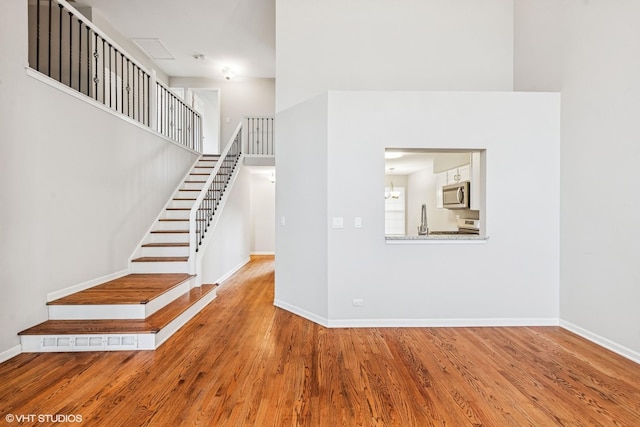stairway with visible vents, baseboards, wood finished floors, and a high ceiling
