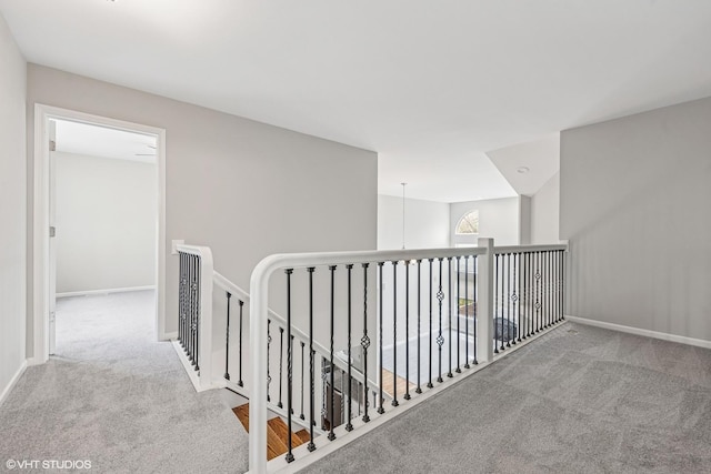 hall featuring carpet flooring, baseboards, and an upstairs landing