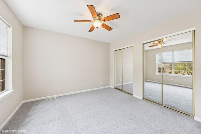unfurnished bedroom featuring visible vents, baseboards, carpet, ceiling fan, and two closets
