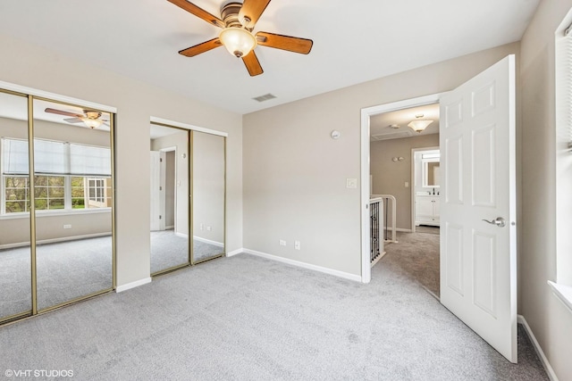 unfurnished bedroom featuring visible vents, baseboards, carpet flooring, and two closets