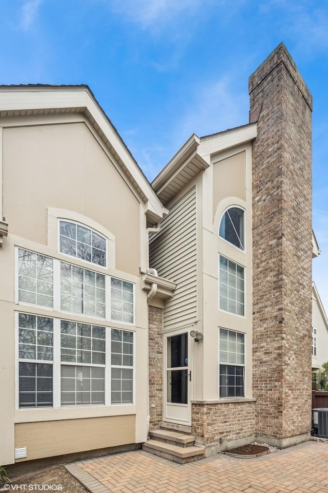 back of property with cooling unit, entry steps, a chimney, and stucco siding