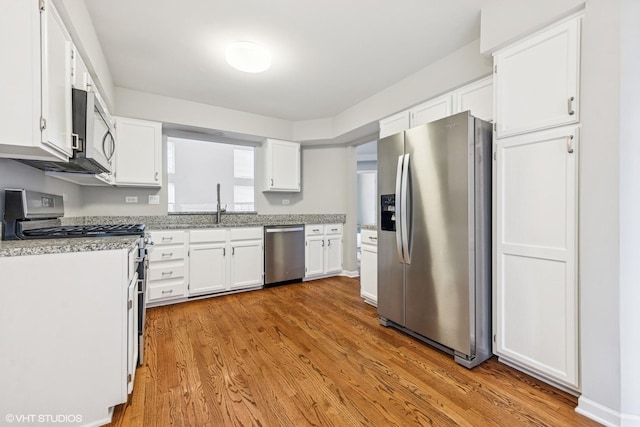 kitchen with white cabinets, appliances with stainless steel finishes, wood finished floors, and a sink