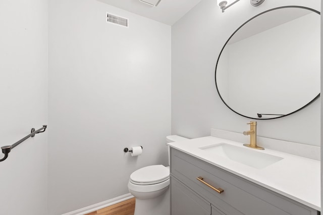 half bathroom featuring visible vents, toilet, wood finished floors, baseboards, and vanity