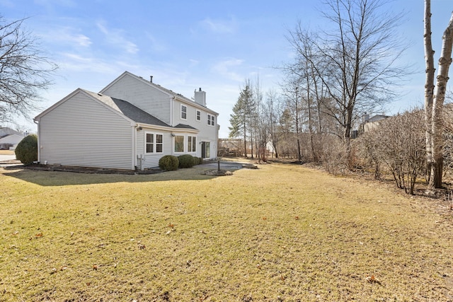 back of house featuring a yard, a chimney, and a shingled roof