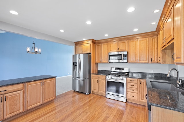 kitchen featuring a sink, stainless steel appliances, dark stone counters, light wood-style floors, and an inviting chandelier