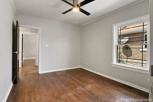 spare room featuring dark wood-type flooring, ceiling fan, baseboards, and crown molding