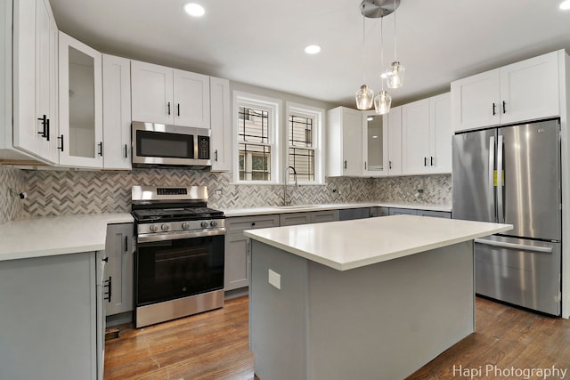 kitchen featuring appliances with stainless steel finishes, a sink, dark wood finished floors, light countertops, and backsplash