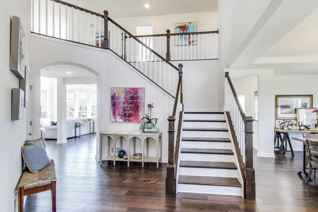stairway with arched walkways, baseboards, a towering ceiling, and wood finished floors