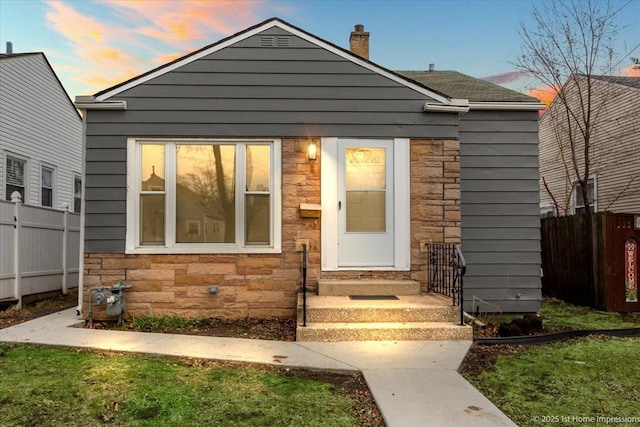 view of front of home featuring stone siding, entry steps, and fence