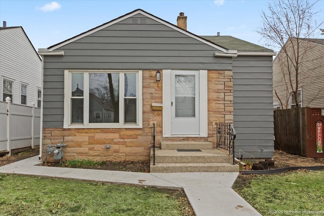 bungalow-style house featuring fence, stone siding, and a chimney