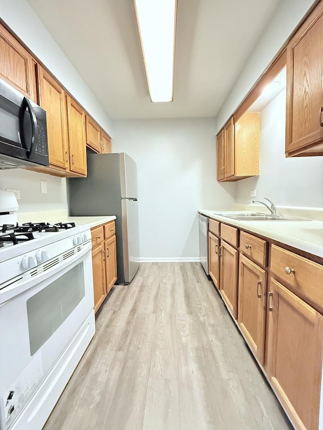 kitchen featuring baseboards, light countertops, light wood-style flooring, stainless steel appliances, and a sink