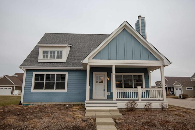 view of front of house with board and batten siding, a chimney, covered porch, and a shingled roof