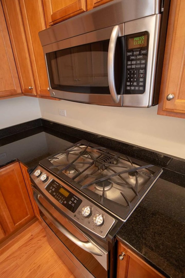 details with brown cabinetry, dark stone countertops, stainless steel appliances, and light wood-style flooring