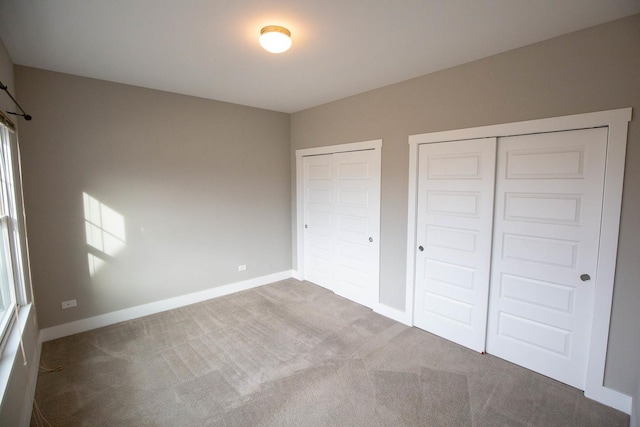 unfurnished bedroom with carpet flooring, two closets, and baseboards