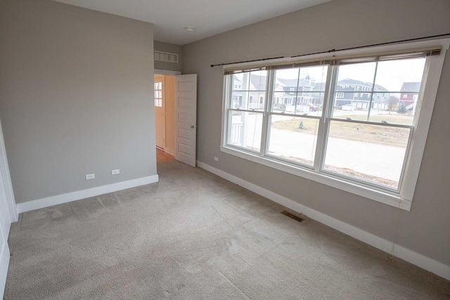 carpeted empty room featuring a wealth of natural light, visible vents, and baseboards