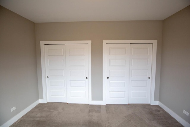 unfurnished bedroom with baseboards, carpet, and multiple closets