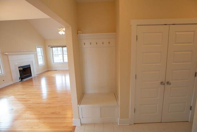 mudroom featuring baseboards, ceiling fan, light wood-type flooring, vaulted ceiling, and a fireplace