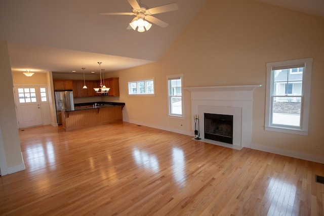 unfurnished living room with a fireplace with flush hearth, a healthy amount of sunlight, light wood-type flooring, and baseboards