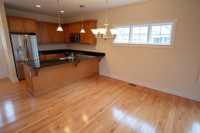 kitchen featuring light wood-style flooring, a kitchen breakfast bar, stainless steel appliances, a peninsula, and brown cabinetry