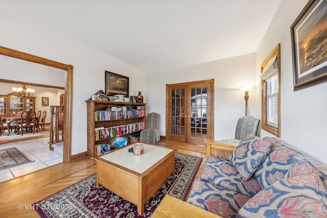 living area featuring french doors, a notable chandelier, baseboards, and light wood-style floors