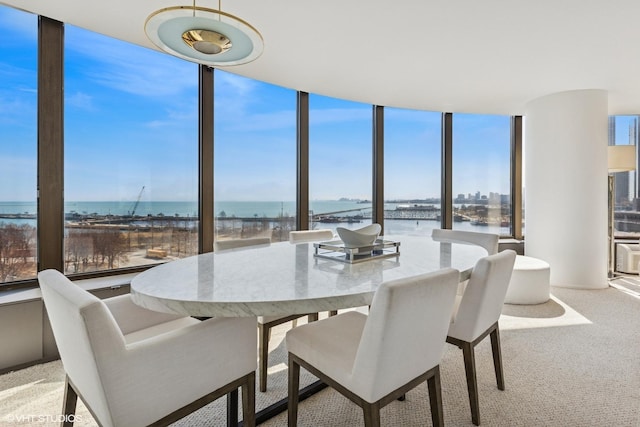 dining area featuring light colored carpet, a wall of windows, and a water view