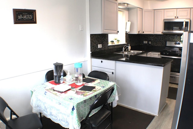 kitchen featuring a sink, dark countertops, backsplash, appliances with stainless steel finishes, and a peninsula