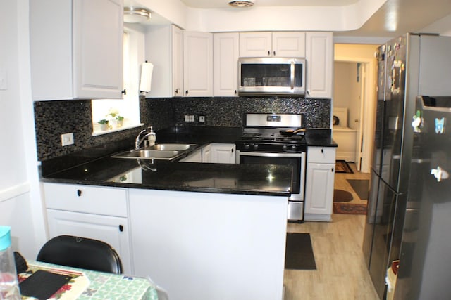 kitchen featuring a peninsula, white cabinets, appliances with stainless steel finishes, and a sink