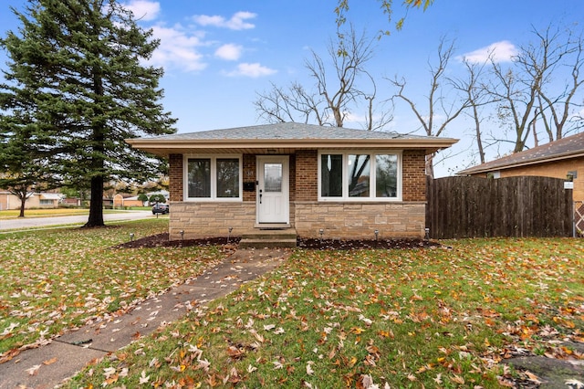 view of front of home with stone siding, a front lawn, and fence