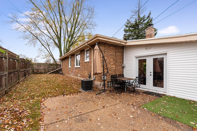 back of property with a fenced backyard, central AC, a chimney, french doors, and brick siding