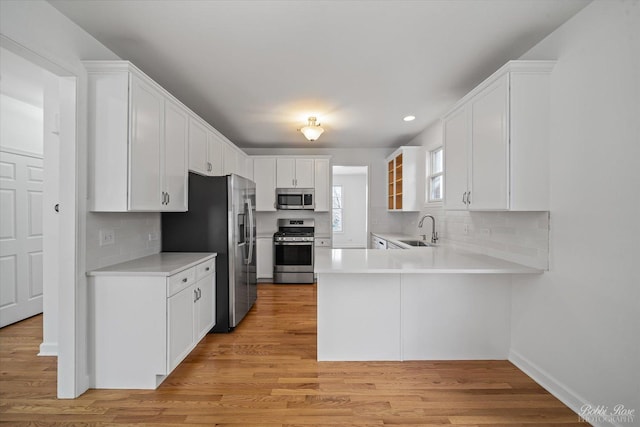 kitchen featuring a sink, appliances with stainless steel finishes, a peninsula, white cabinets, and light countertops