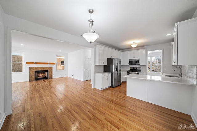 kitchen with light wood finished floors, open floor plan, light countertops, appliances with stainless steel finishes, and a sink