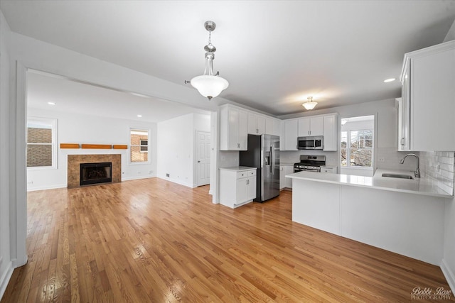 kitchen featuring a sink, open floor plan, stainless steel appliances, light wood finished floors, and light countertops