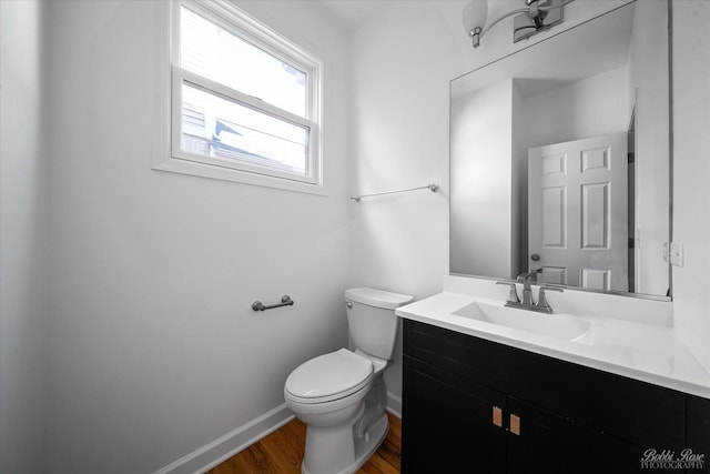 half bath with baseboards, toilet, wood finished floors, and vanity