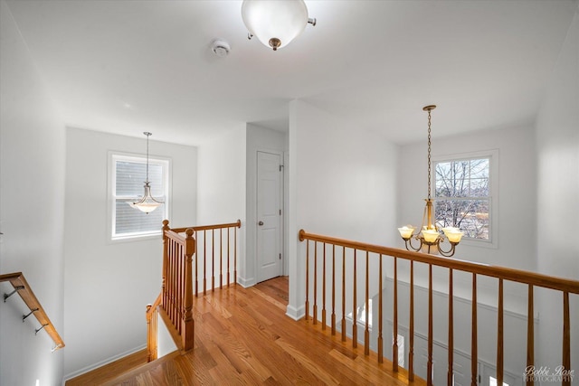 corridor with wood finished floors, an upstairs landing, baseboards, and a chandelier