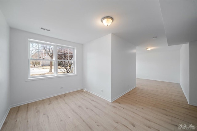 empty room with light wood-style floors, visible vents, and baseboards