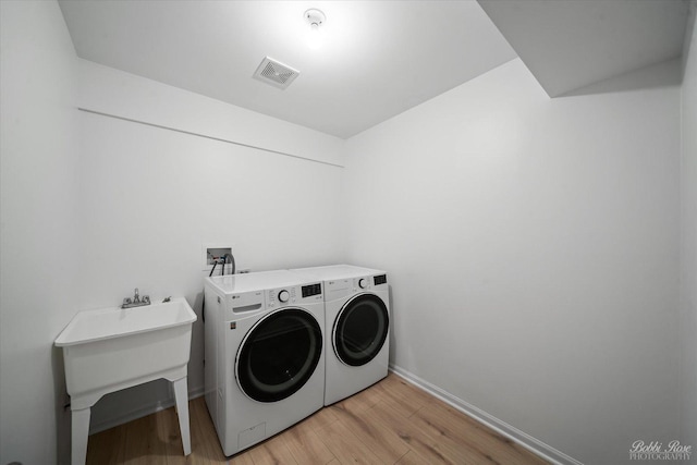 washroom with visible vents, baseboards, laundry area, light wood-style flooring, and washer and clothes dryer