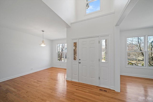 foyer entrance featuring visible vents, baseboards, light wood-style floors, and a high ceiling