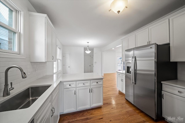 kitchen featuring a peninsula, stainless steel fridge with ice dispenser, a sink, decorative backsplash, and white cabinetry