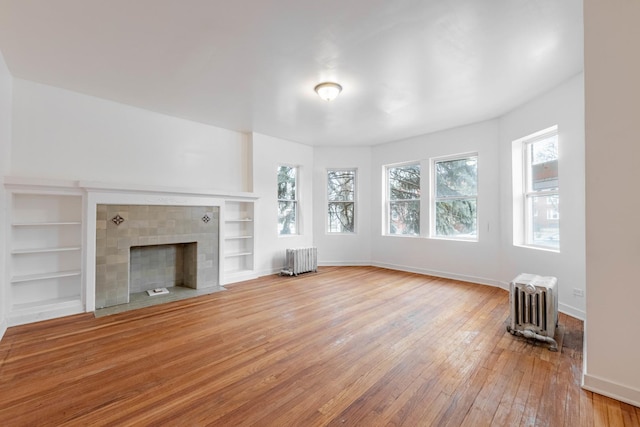 unfurnished living room featuring baseboards, wood-type flooring, radiator, and a tiled fireplace