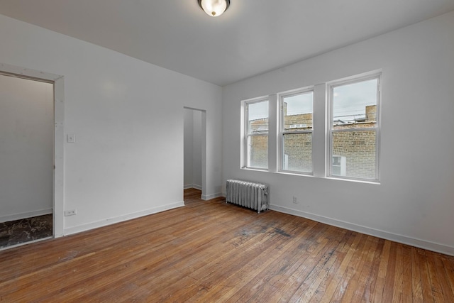 empty room featuring radiator, baseboards, and hardwood / wood-style flooring