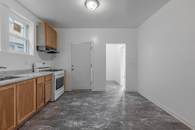 kitchen with white range with gas stovetop, brown cabinetry, under cabinet range hood, and a sink