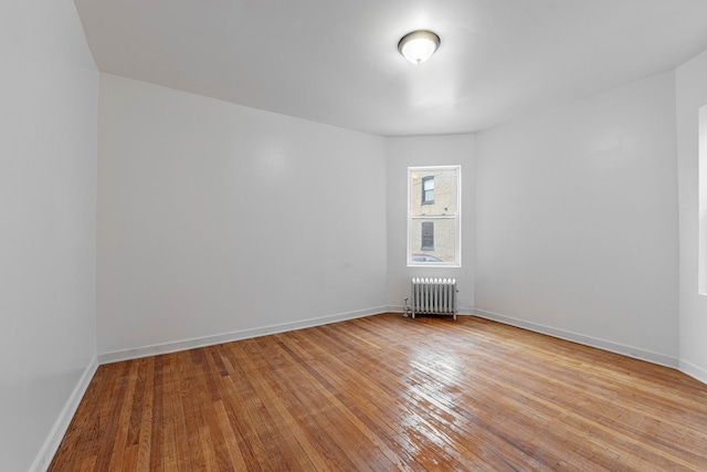 empty room featuring baseboards, radiator heating unit, and light wood finished floors