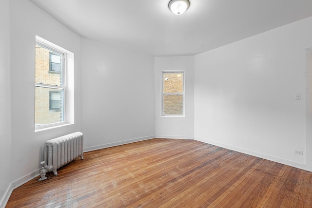 unfurnished room featuring baseboards, radiator, and light wood finished floors