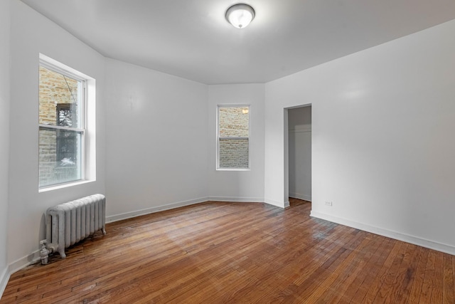 empty room featuring radiator heating unit, baseboards, and hardwood / wood-style floors