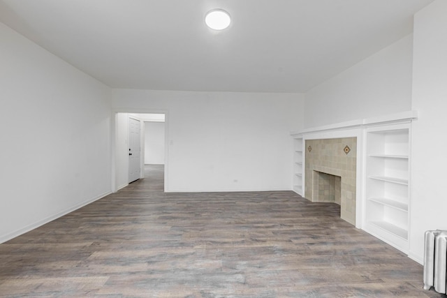 unfurnished living room featuring built in features, radiator, wood finished floors, and a tiled fireplace